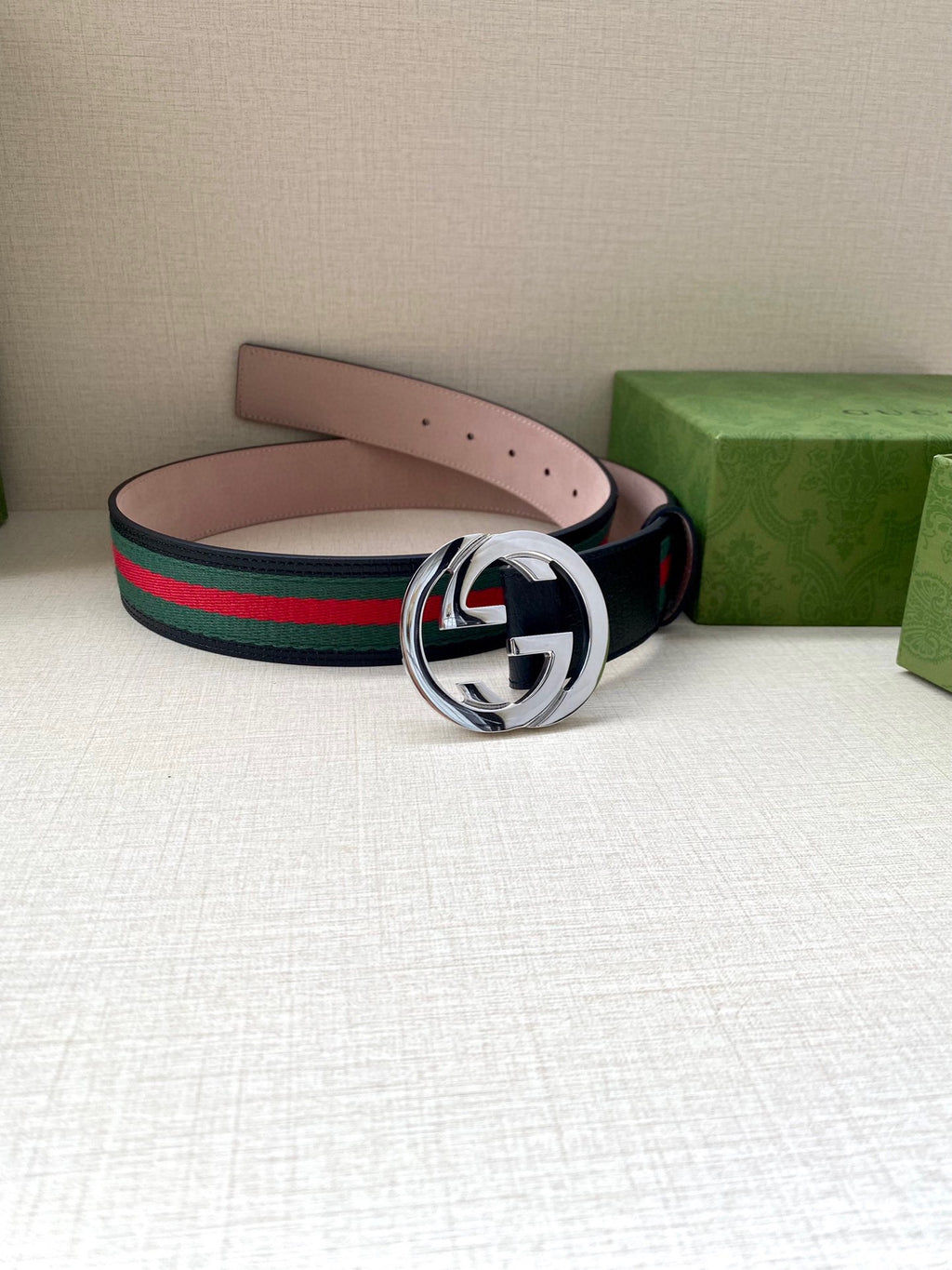 Gucci belt on display: dark blue strap with green-red stripe web and silver-tone buckle.
