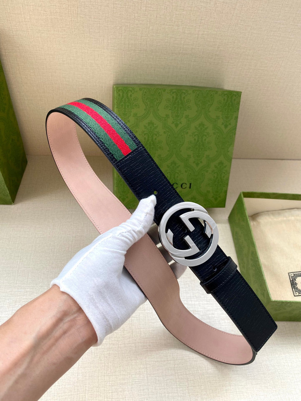 Gucci belt being held: dark blue strap with silver-tone double-G buckle and green-red stripe.