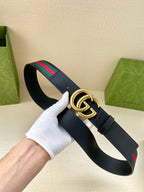 Gucci belt with dark navy strap, gold double-G buckle, green/red web stripe detail.
