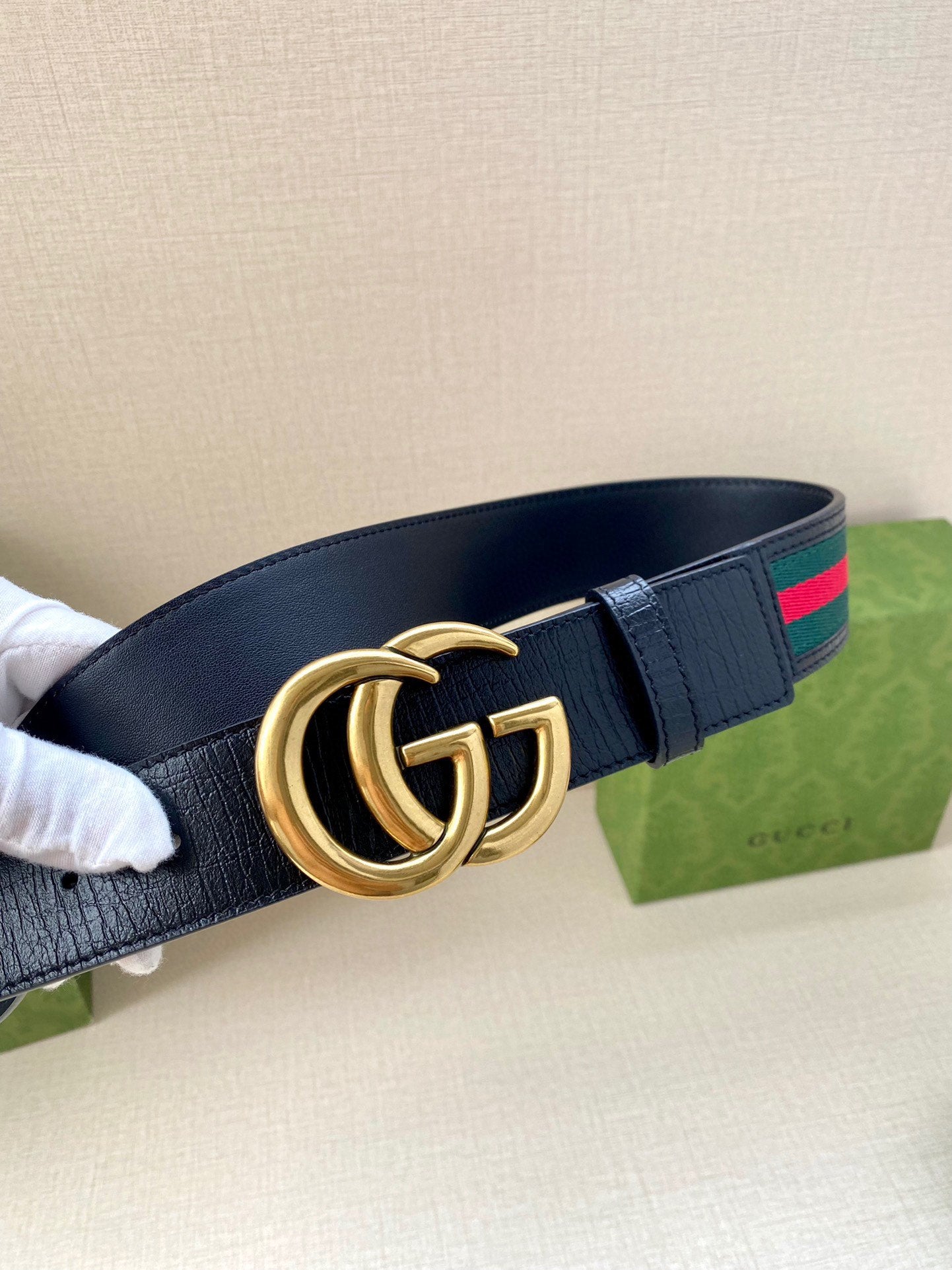 Gucci belt, side view: dark navy strap with gold double-G buckle and green/red web stripe.