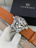 Orange leather belt close-up with silver-toned Medusa buckle held in white glove