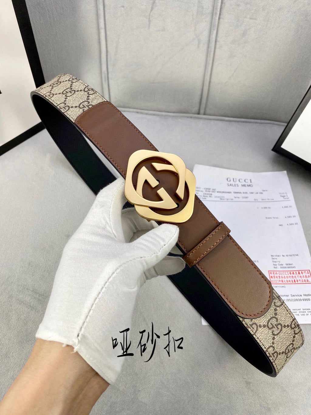 Gucci belt held in hand with GG canvas and brown leather, gold-tone interlocking buckle.