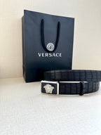 Navy leather belt with embossed texture and gold Medusa buckle, laid flat