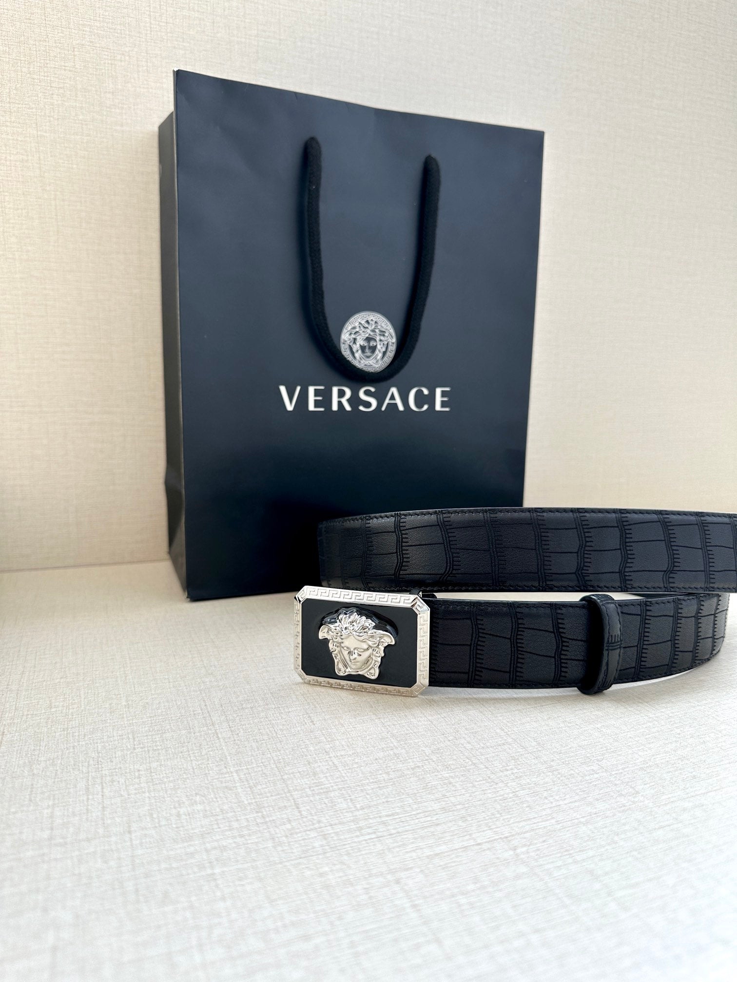Navy leather belt with embossed texture and gold Medusa buckle, laid flat