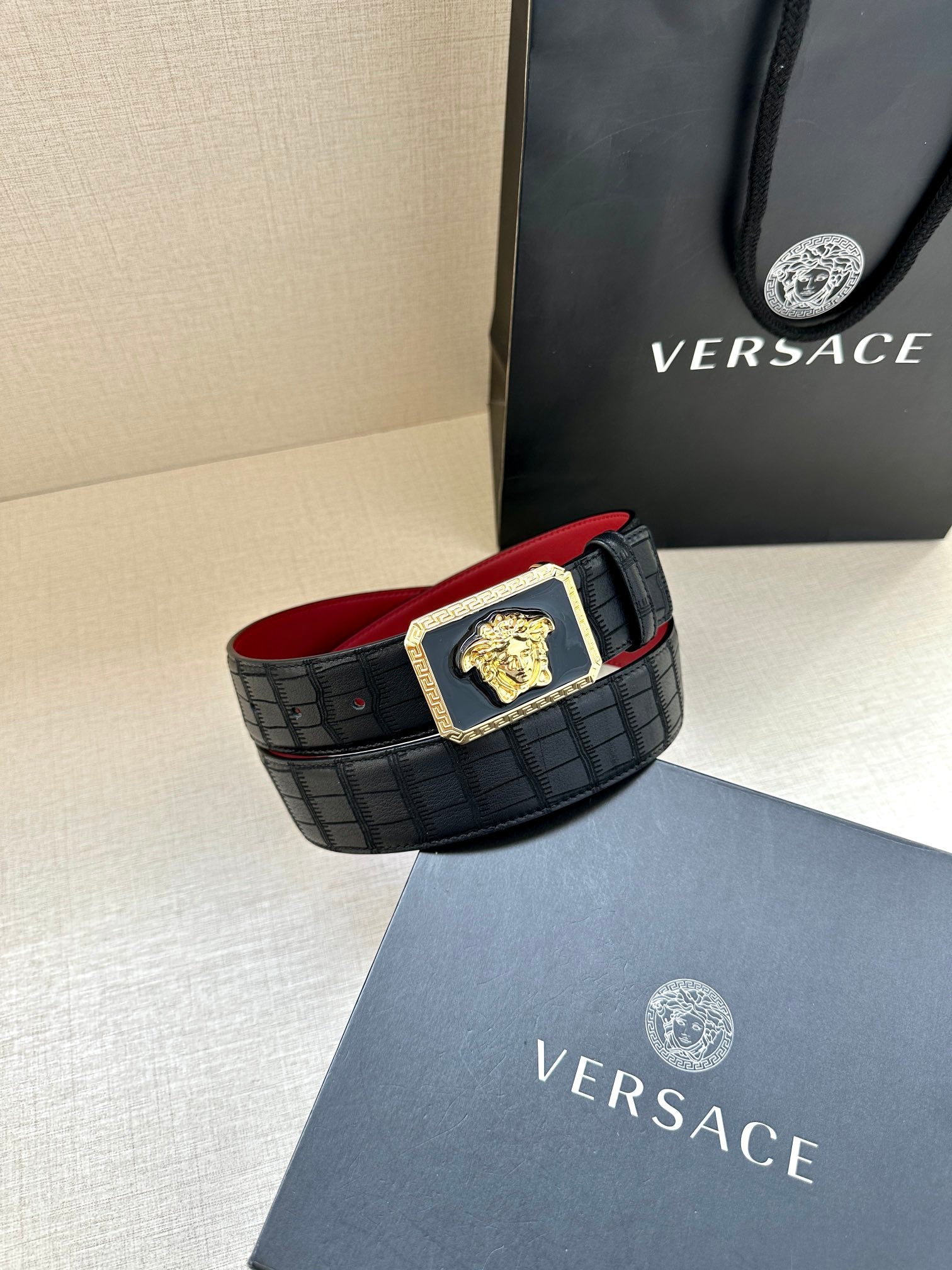 Belt: black textured belt with gold Medusa square buckle and red underside visible.