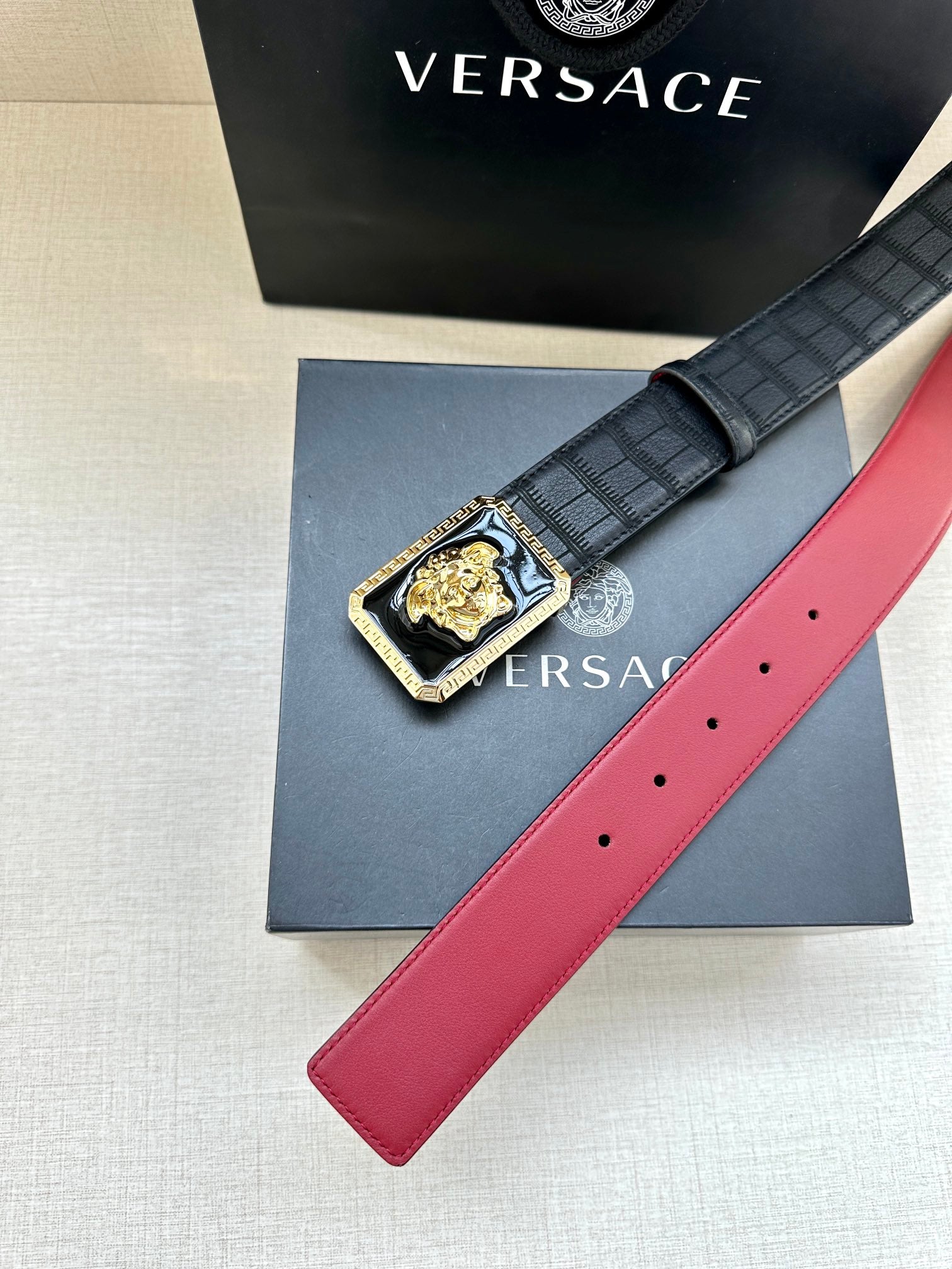 Belt: black strap with gold-edged Medusa buckle and red underside strap end.