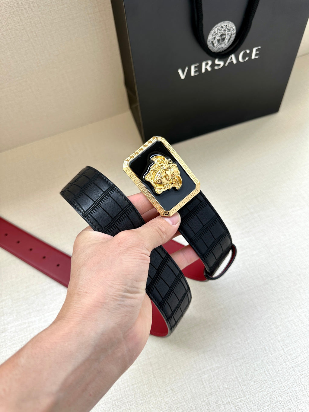 Belt: black textured strap with square Medusa buckle, gold plate and red underside.