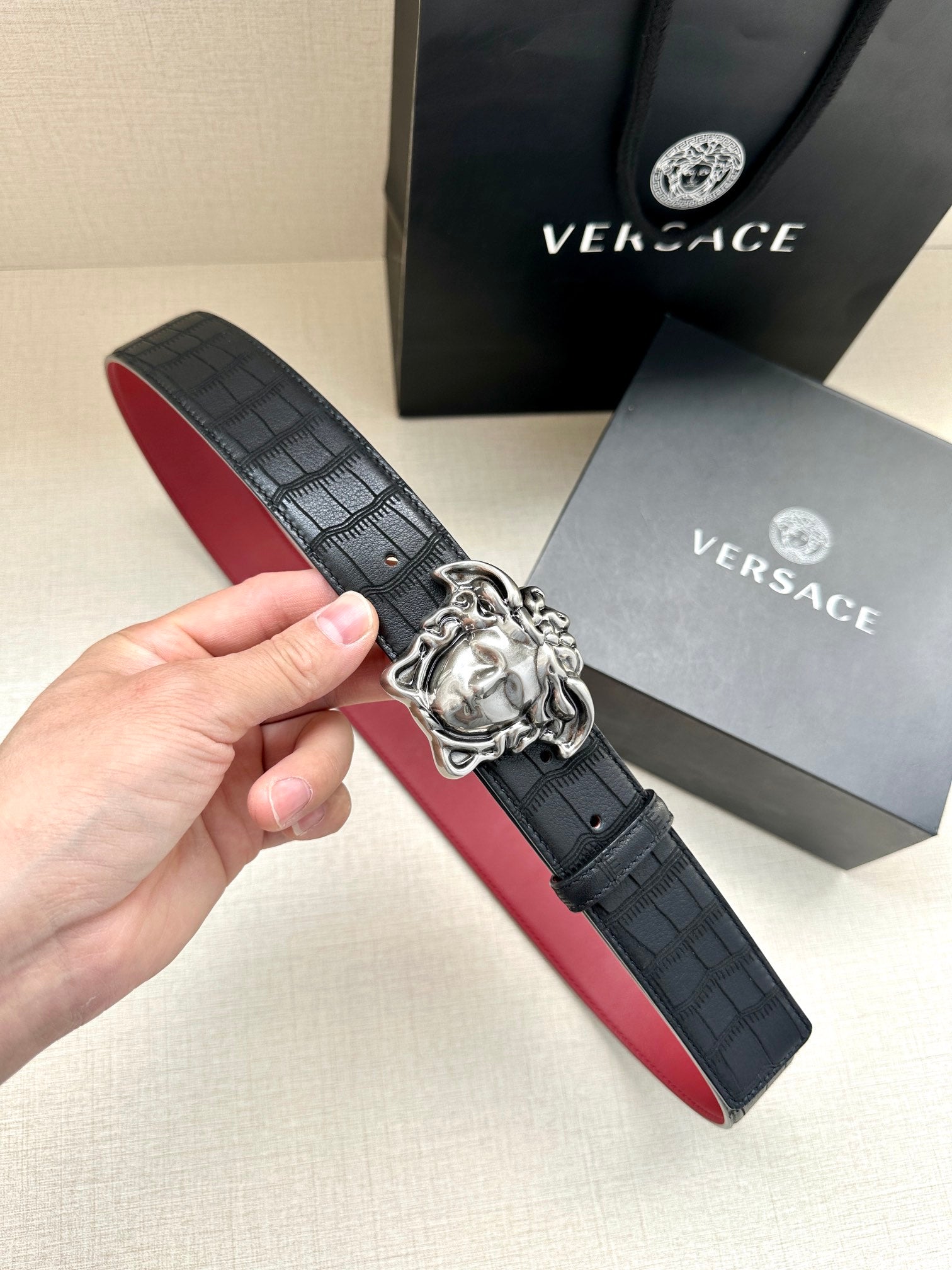 Black leather belt with red underside and silver Medusa-style buckle