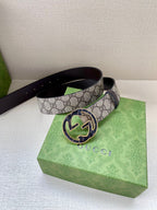 Gucci belt with dark GG monogram strap and round buckle, resting on a bag