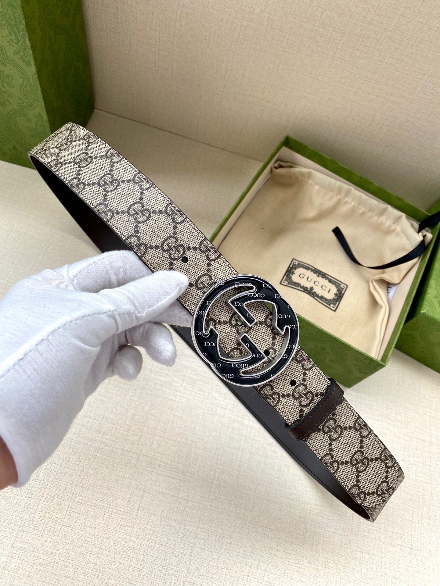 Gucci belt with GG monogram canvas strap and dark metal oval buckle, held in hand