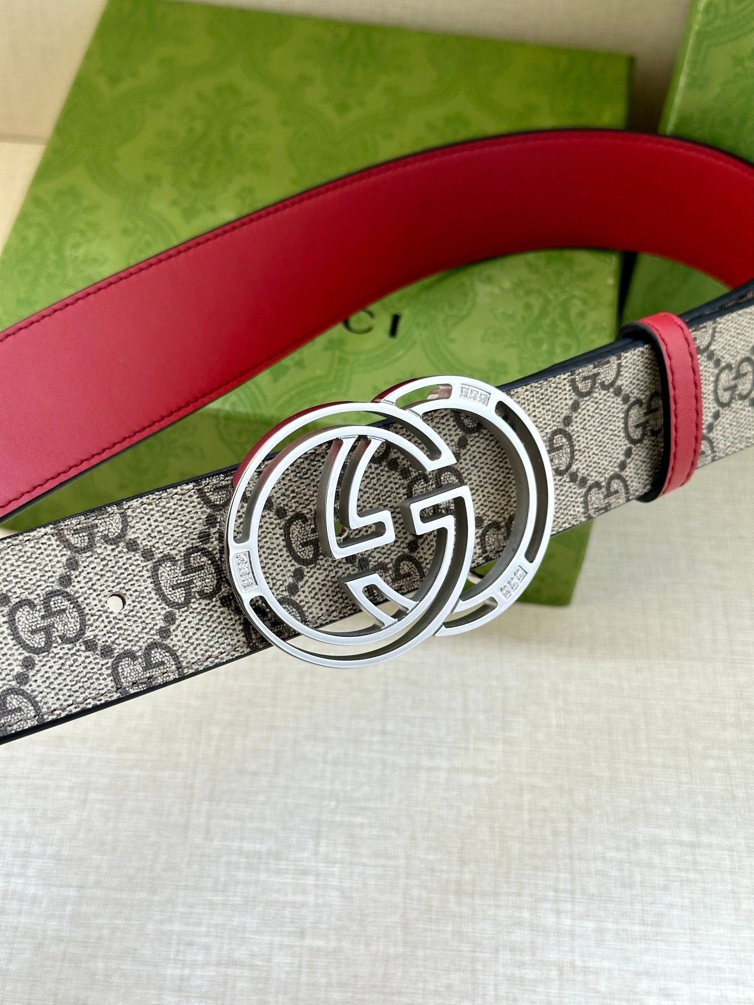 Gucci belt showing gray GG monogram strap, red leather trim, and large silver-tone GG buckle