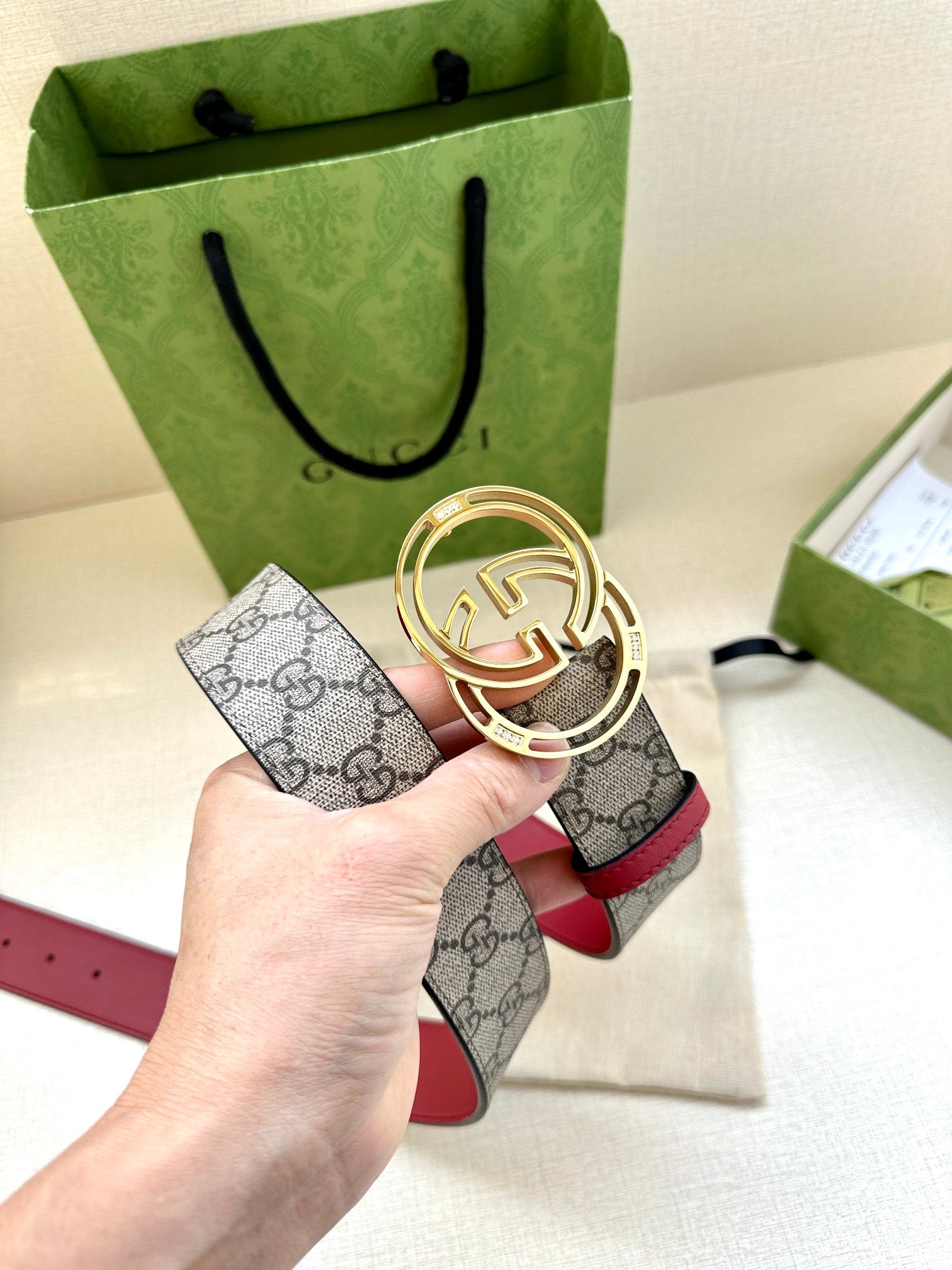 Gucci belt held in hand: gray GG monogram strap with red leather trim and gold-tone GG buckle