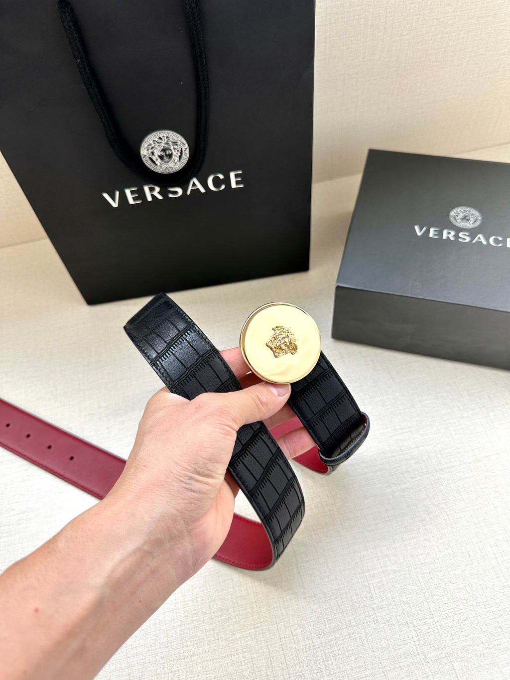 Versace belt with black grid strap and gold medallion buckle, red underside visible