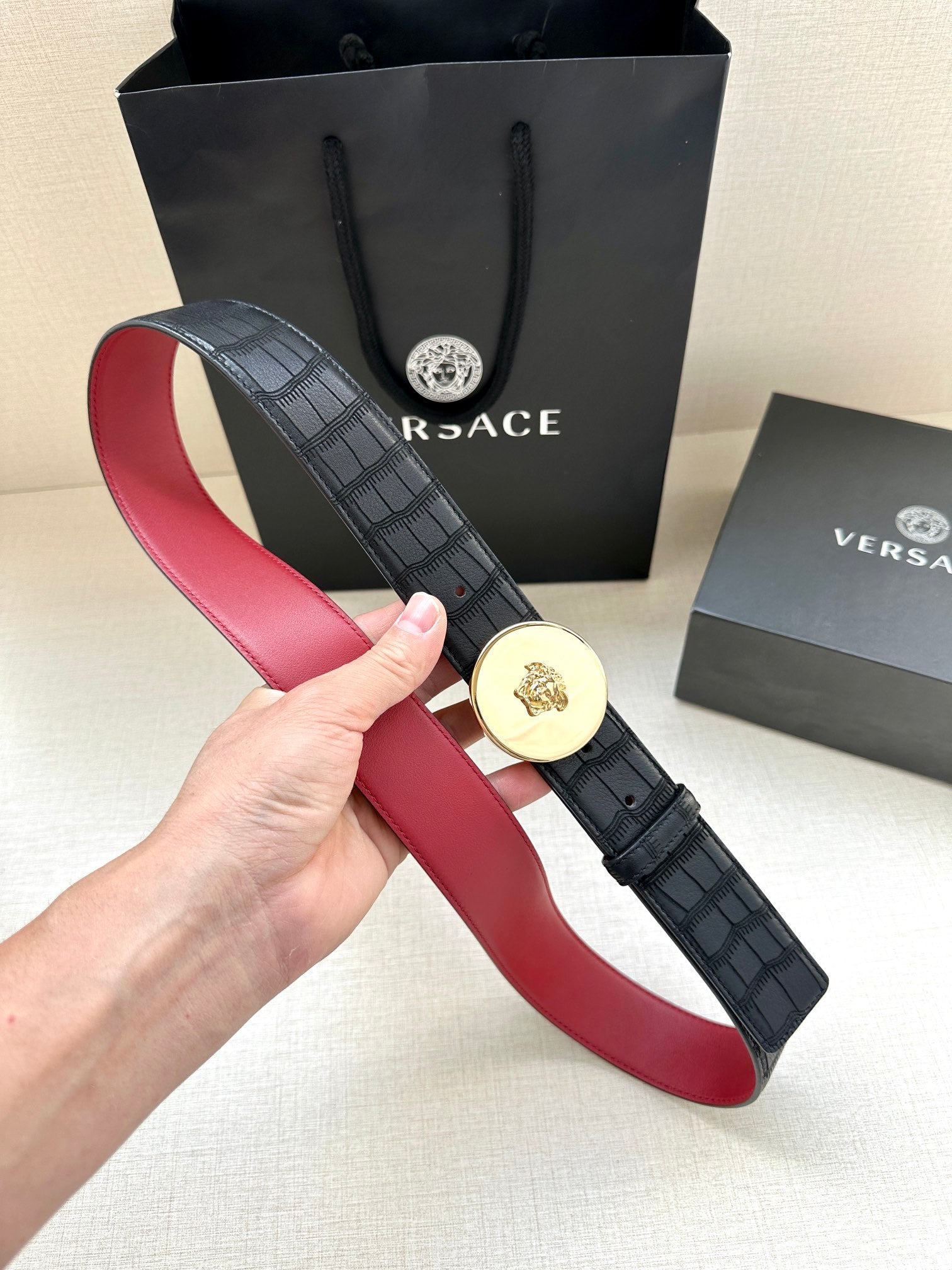 Versace belt held open: black grid strap with gold medallion buckle and red inner band