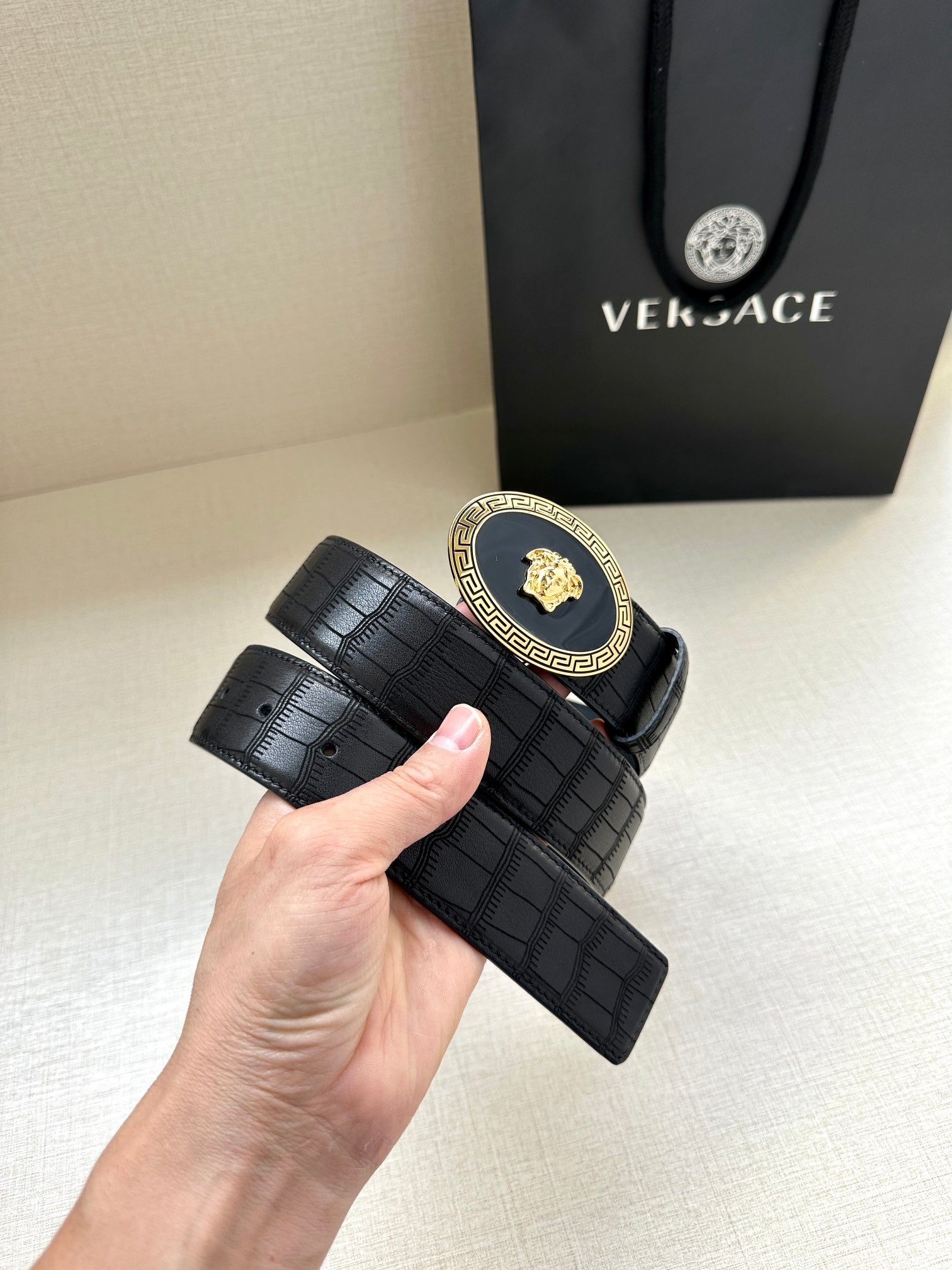 Black embossed leather belt with gold oval medallion buckle and wide strap