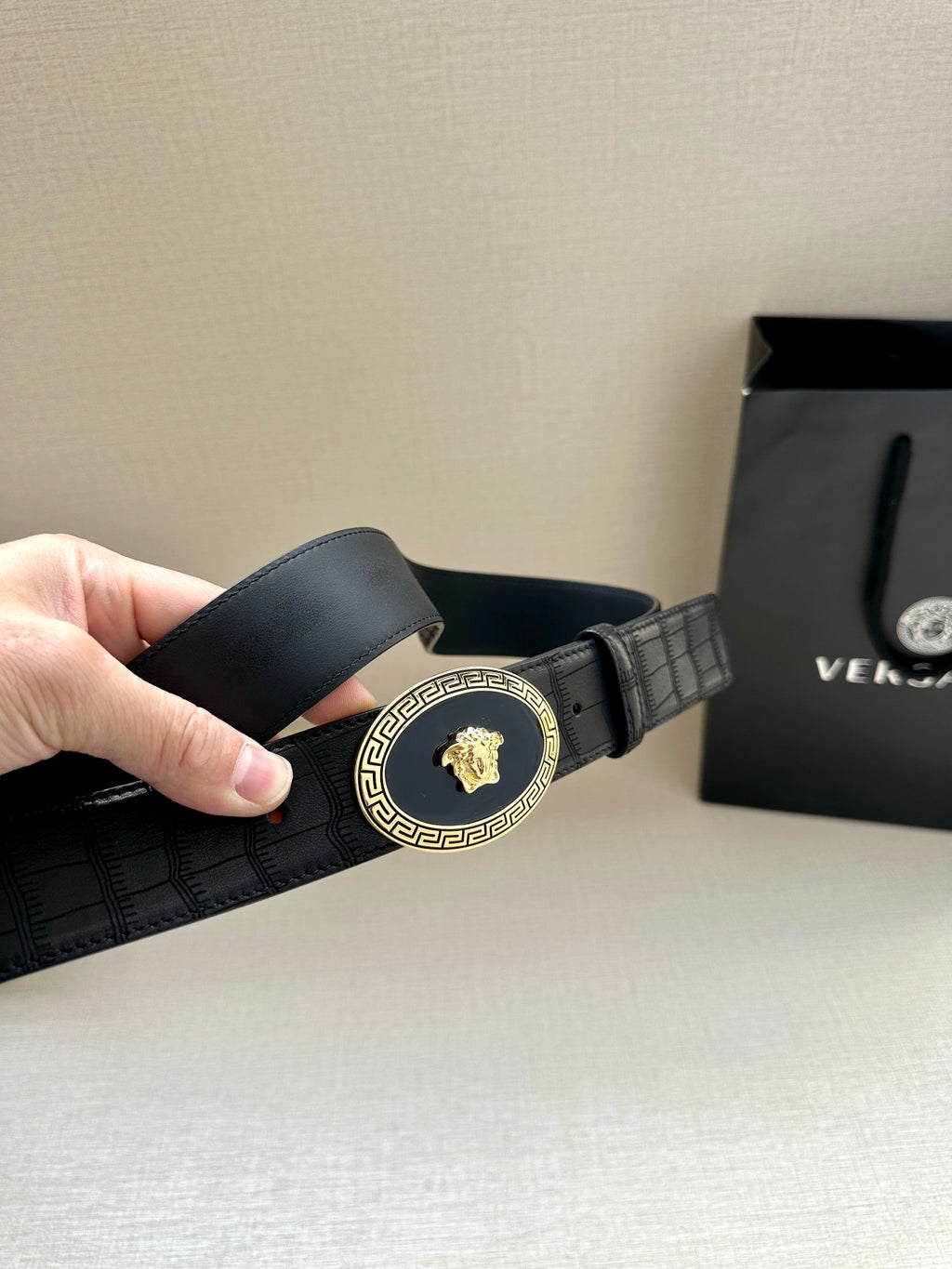 Black leather belt with embossed texture and gold oval buckle, angled view