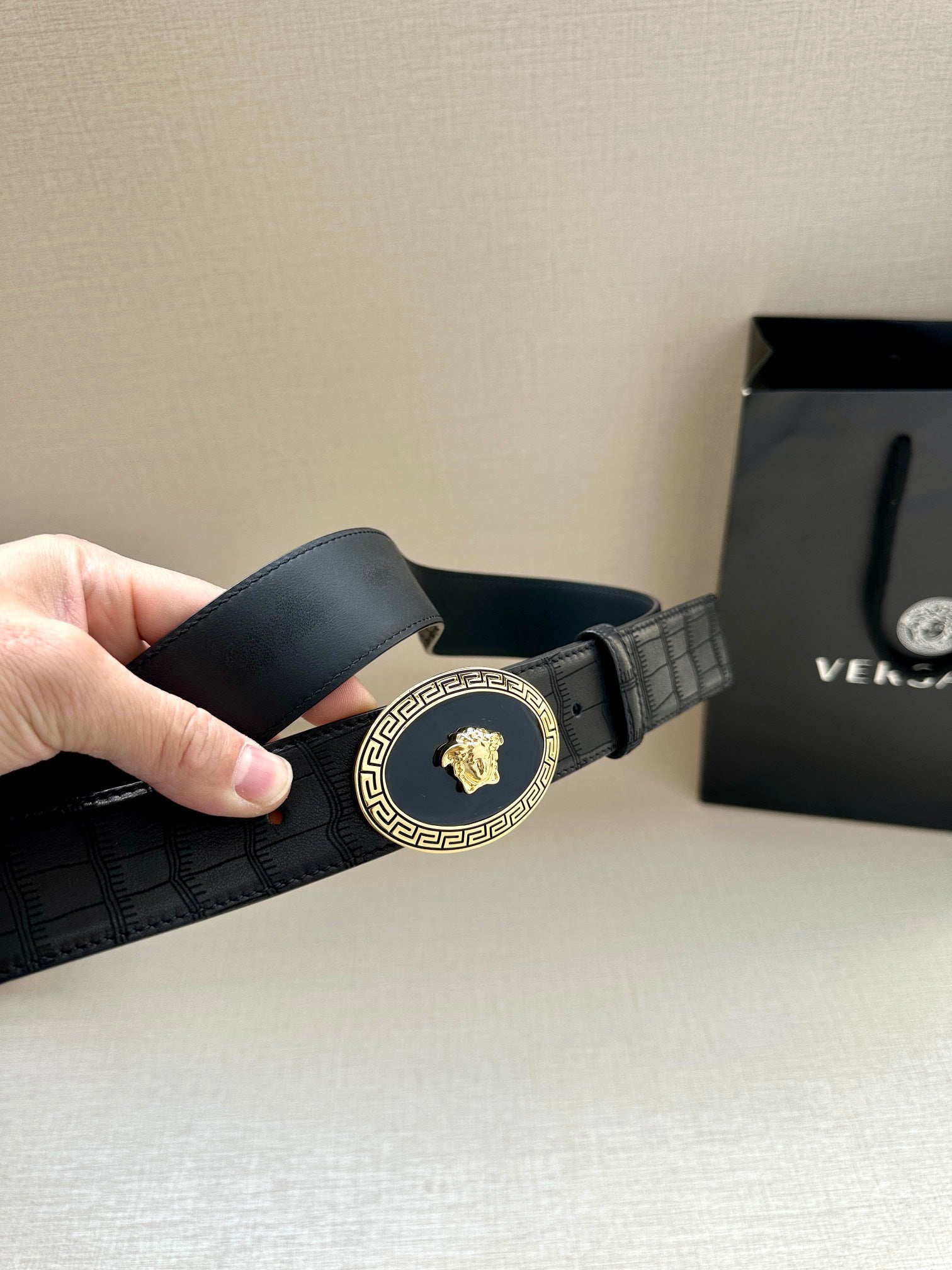 Black leather belt with embossed texture and gold oval buckle, angled view