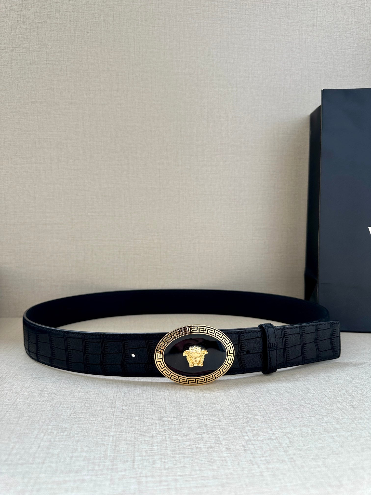 Black embossed leather belt with gold oval medallion buckle and single prong