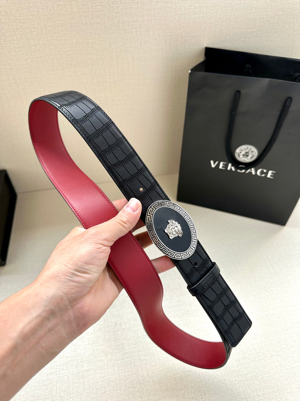 Versace belt held up: black textured strap, round medallion buckle, red underside