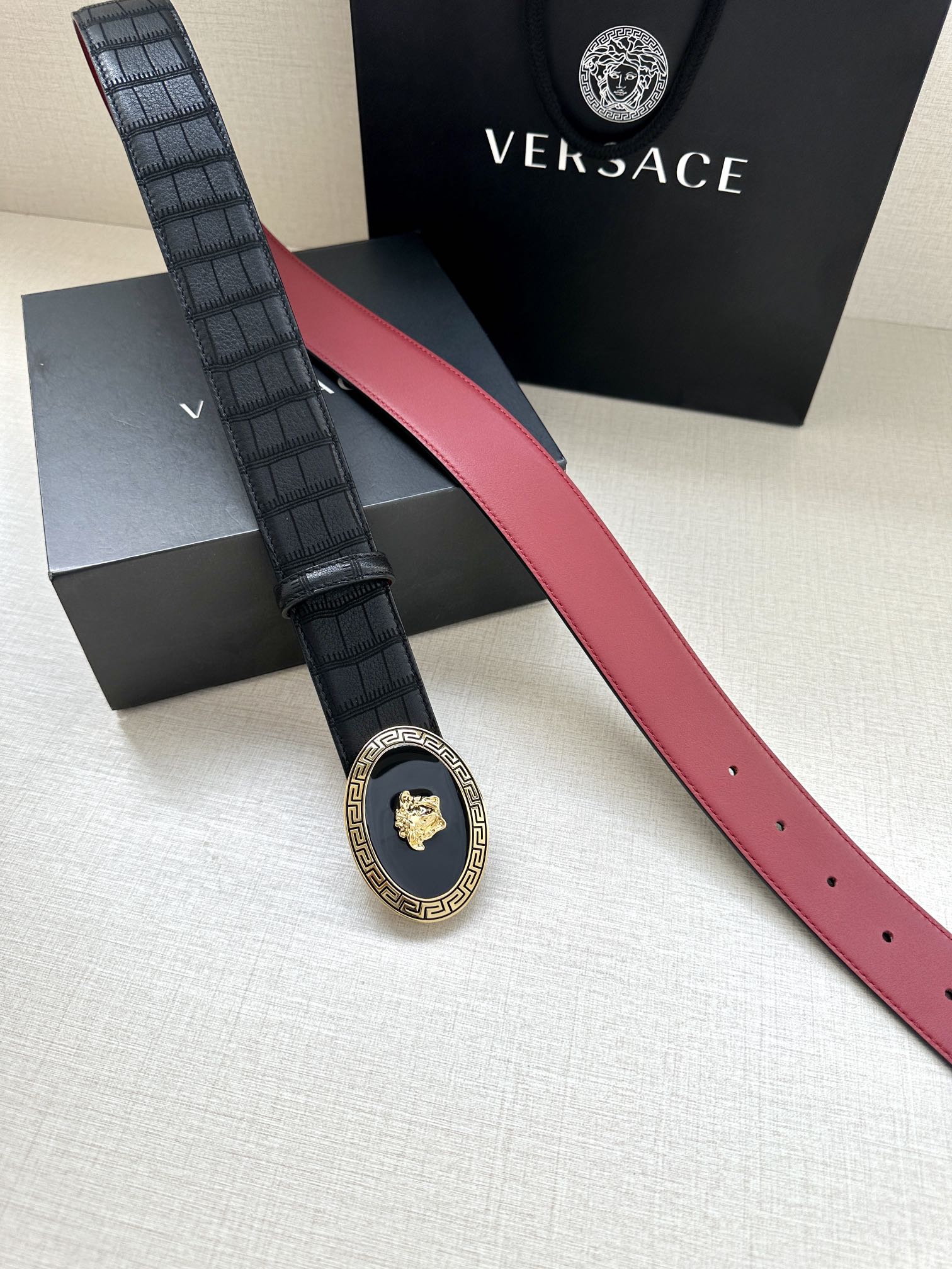 Versace belt laid flat: black textured strap, red interior edge, round gold medallion buckle