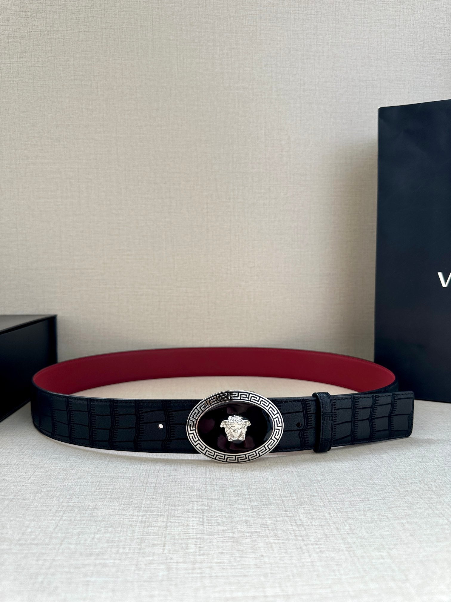 Versace belt with black textured strap and round gold medallion buckle on red back