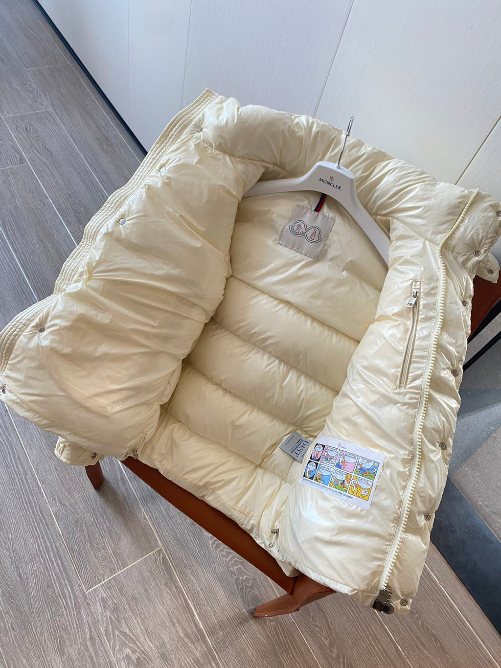 Moncler long cream puffer jacket laid flat with hood, zip, and brand tag inside