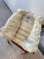 Moncler long cream puffer jacket laid flat with hood, zip, and brand tag inside