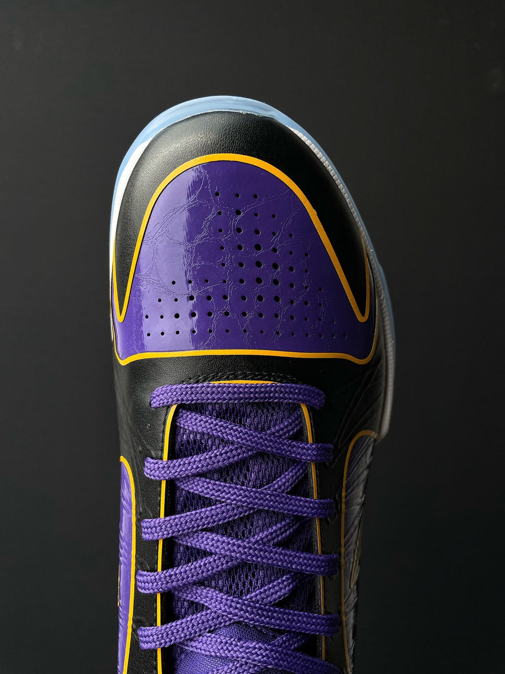 Low-top basketball shoe front side, purple perforated panel, purple laces, yellow edge trim.