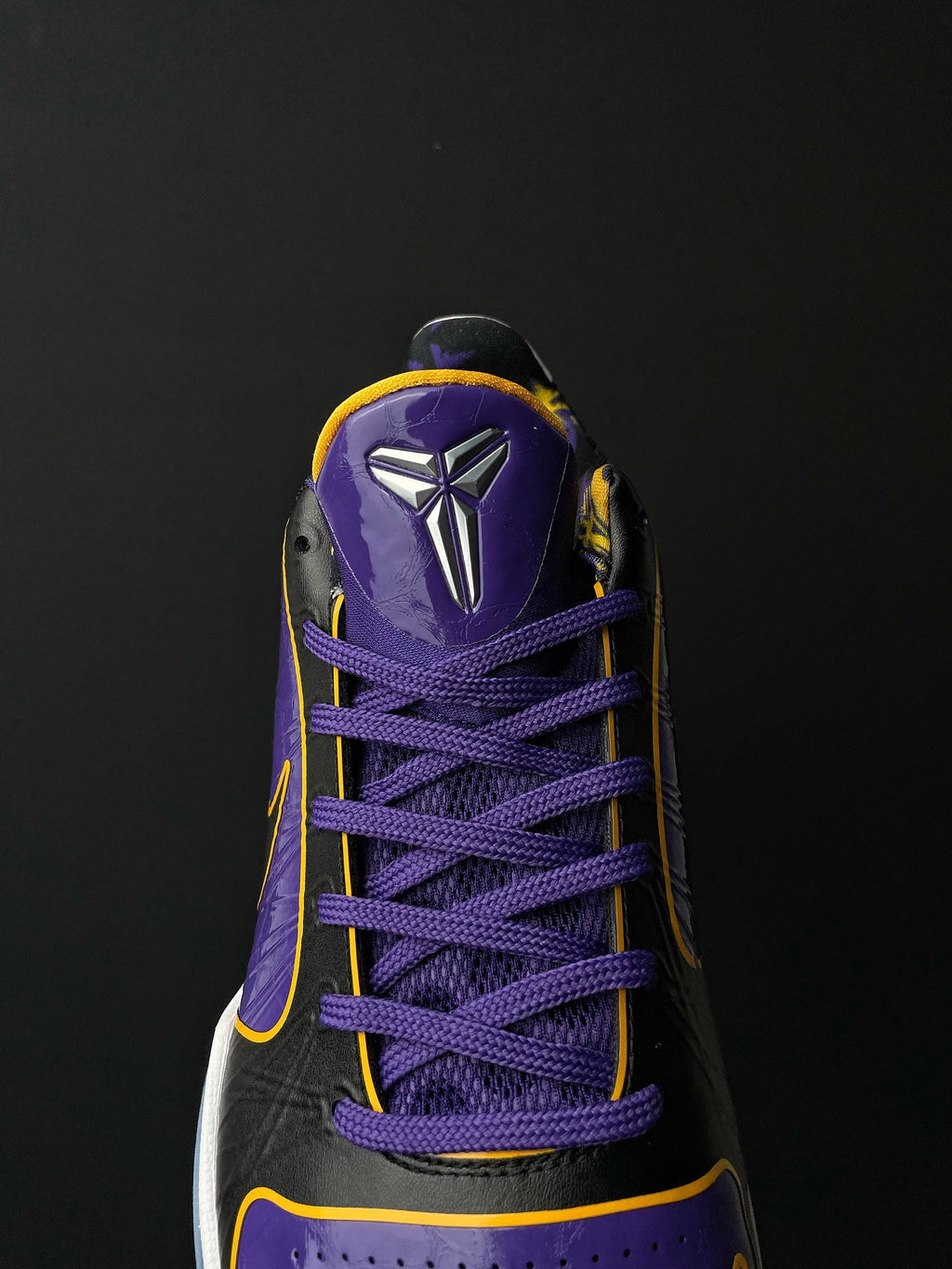 Low-top basketball shoe close-up of toe and laces, purple upper with black overlays.