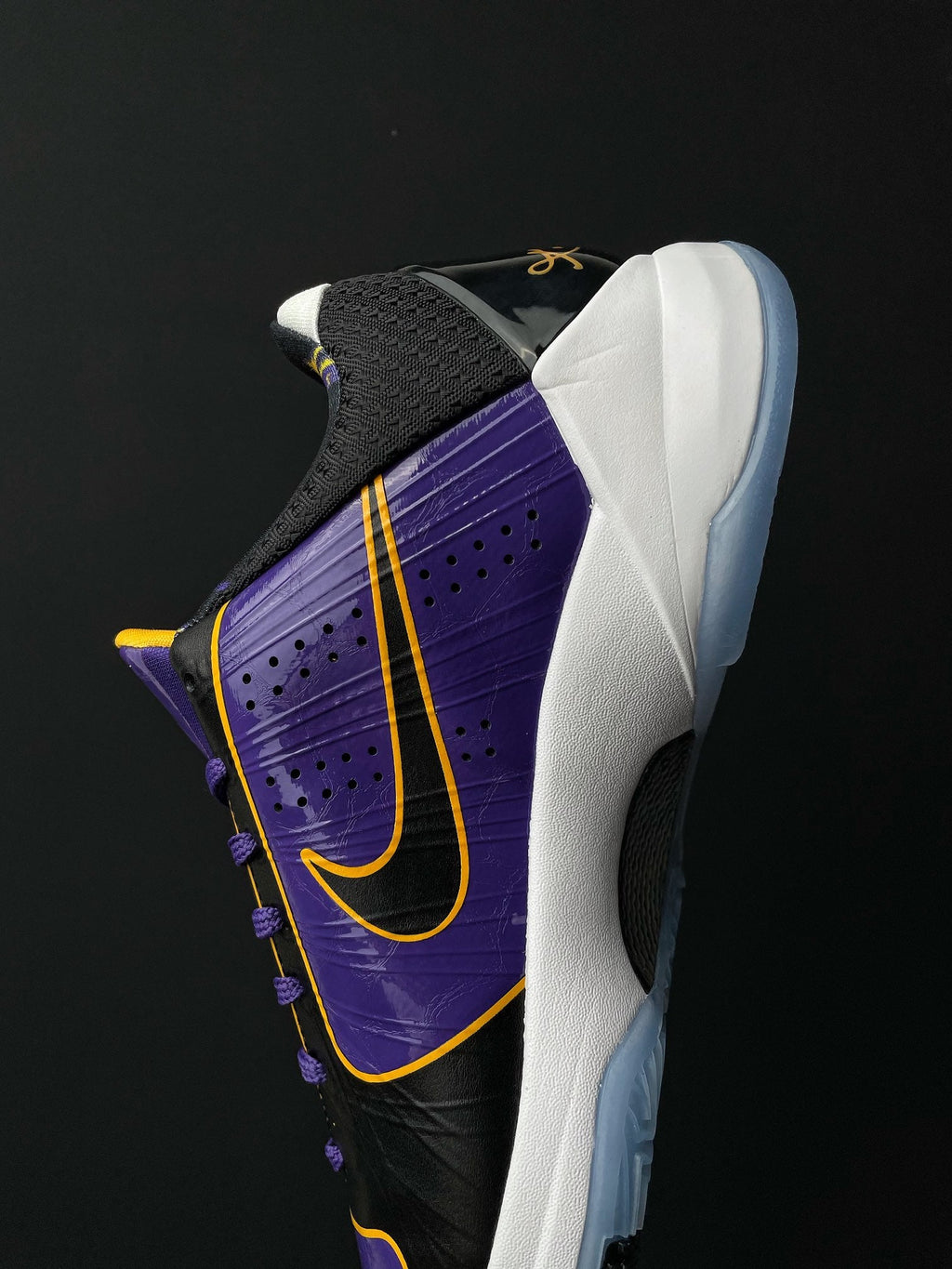 Low-top basketball shoe side view, black upper with purple panel and yellow swoosh detail.