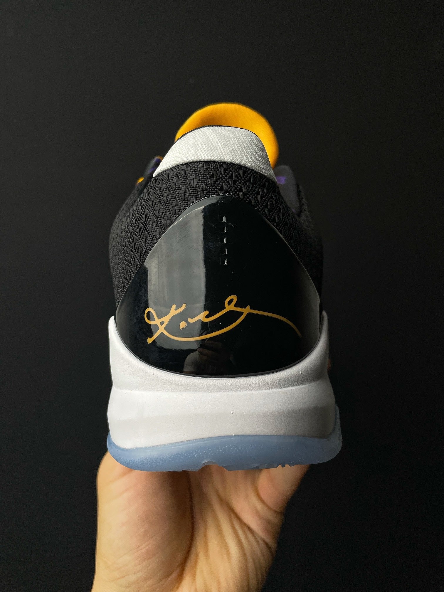 Low-top basketball shoe heel view, black heel tab, white sole, yellow accent script.