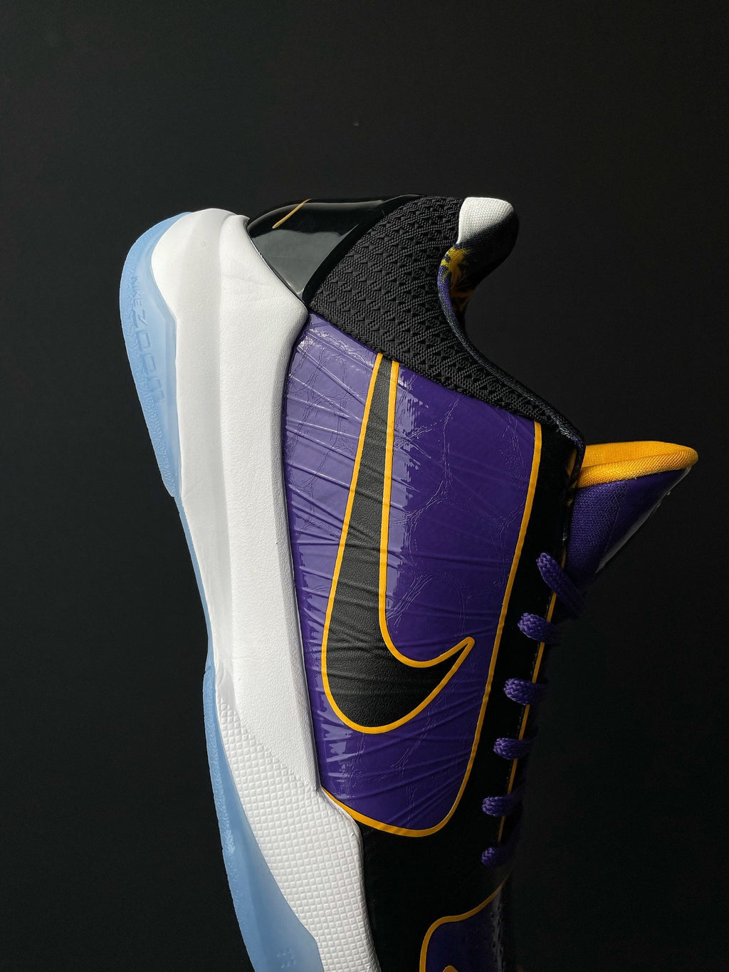 Low-top basketball shoe close-up of side, purple panel with yellow trim, black heel.