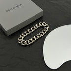 Balenciaga chain bracelet with silver-tone links on black surface, beside white card