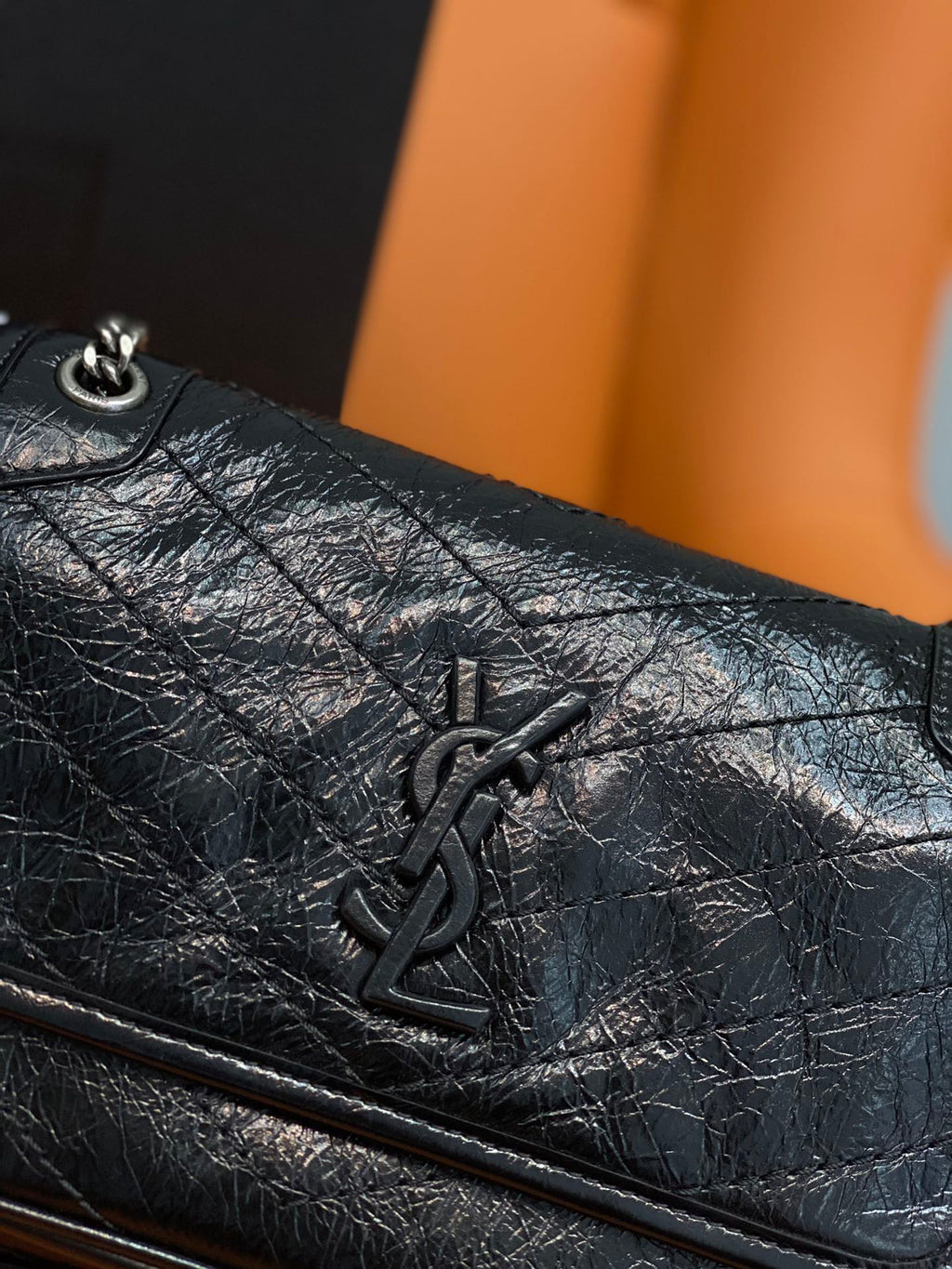 Black leather flap bag close-up with YSL emblem and quilted texture