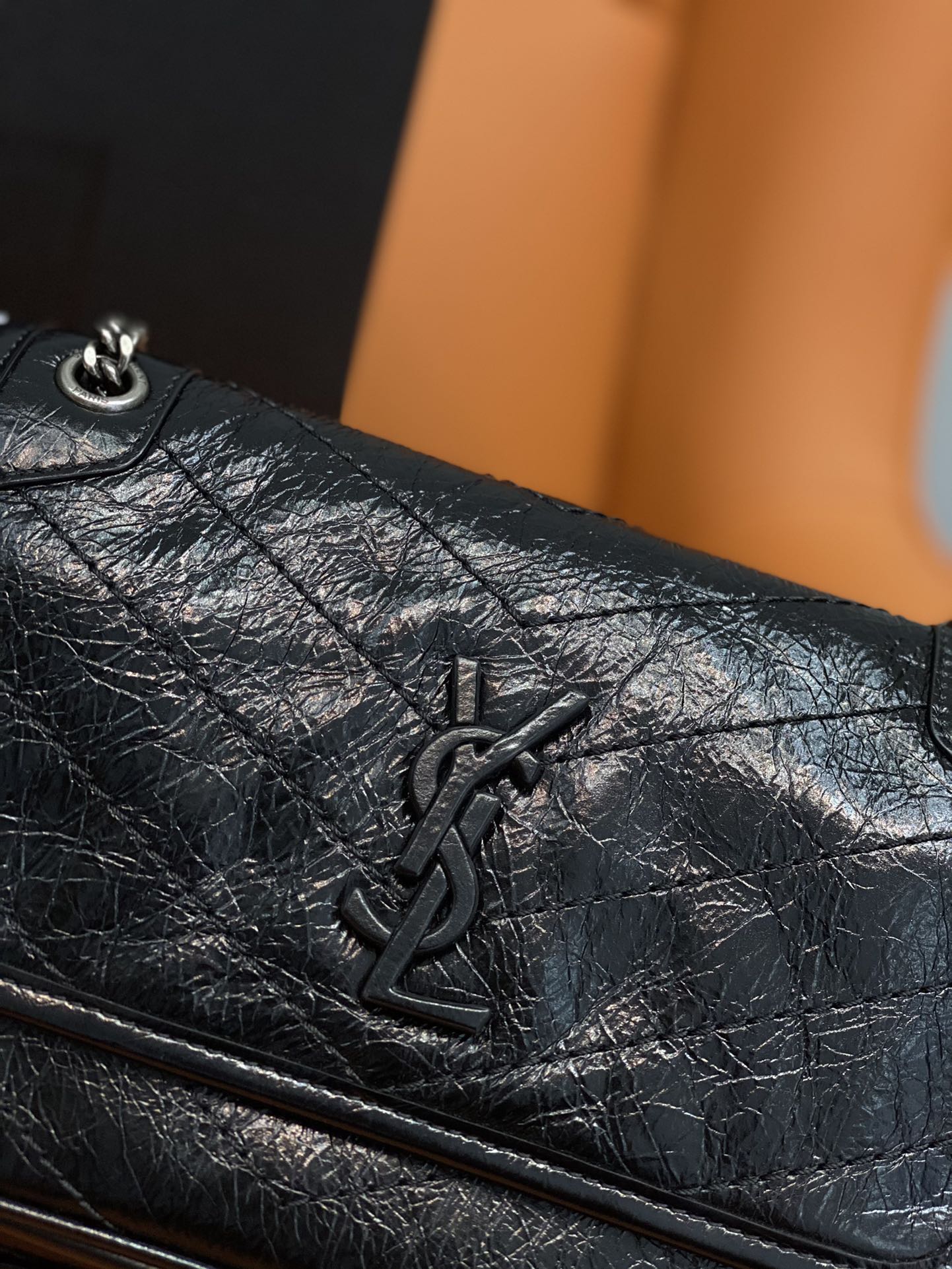 Black leather flap bag close-up with YSL emblem and quilted texture