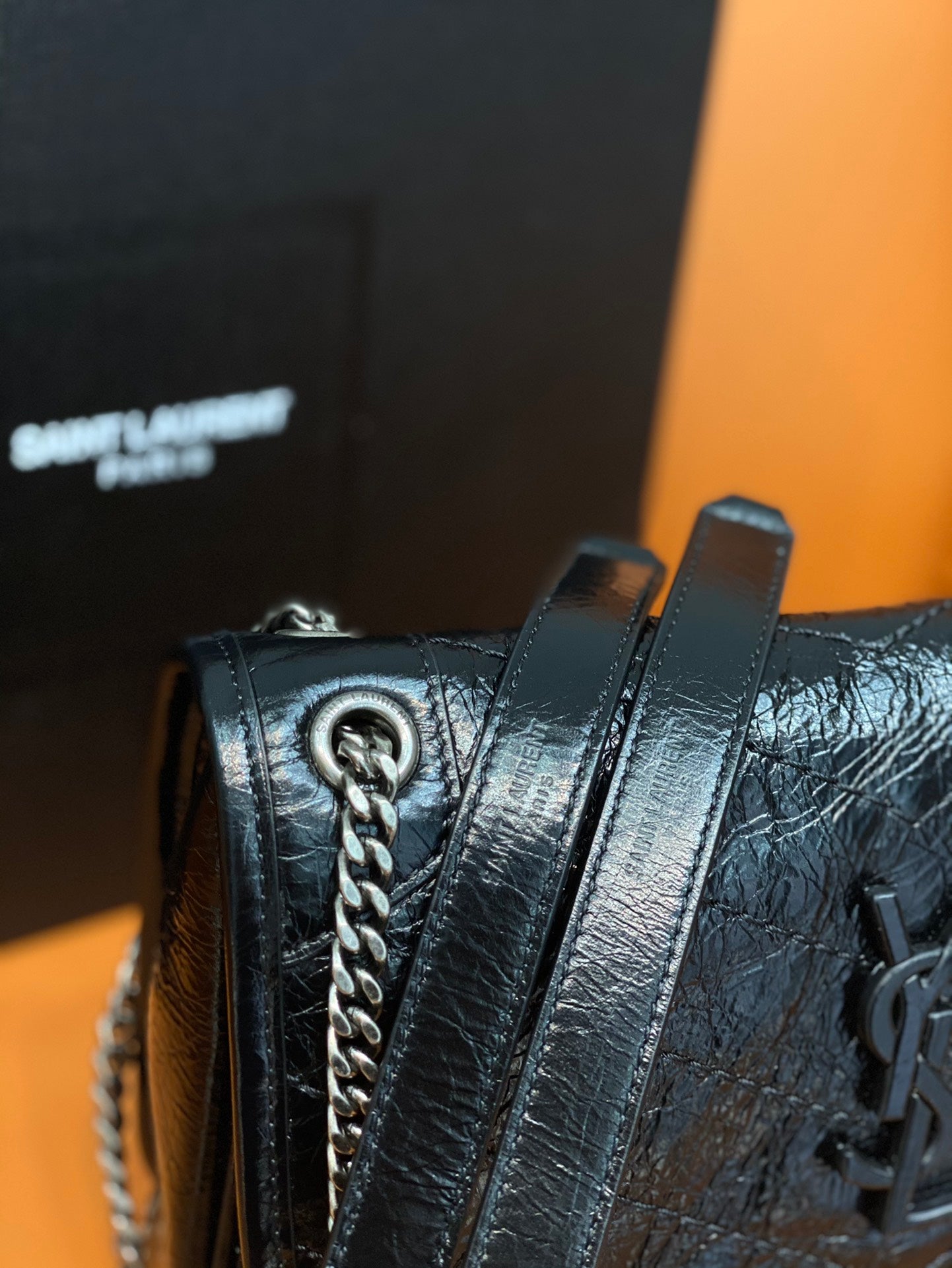 Black quilted leather bag close-up with chain strap and metal emblem hardware