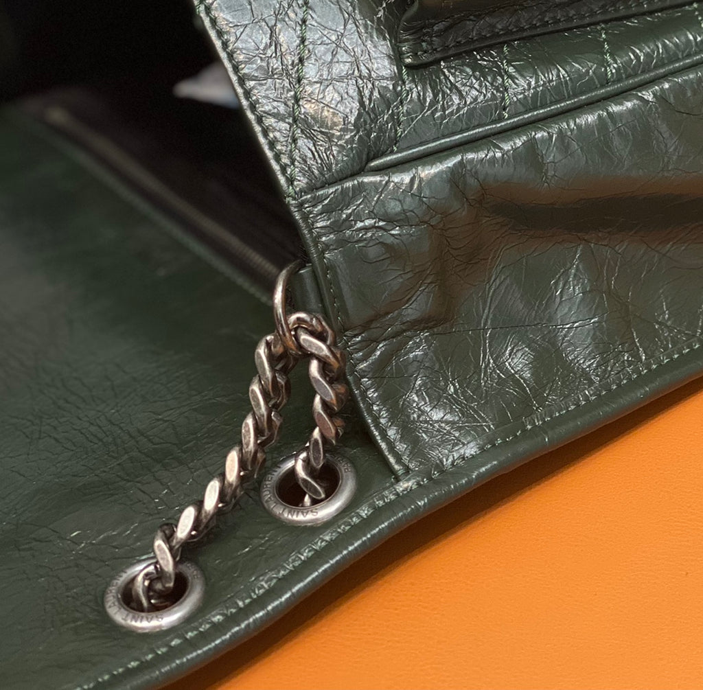 Dark green leather bag corner with chain link hardware and edge stitching