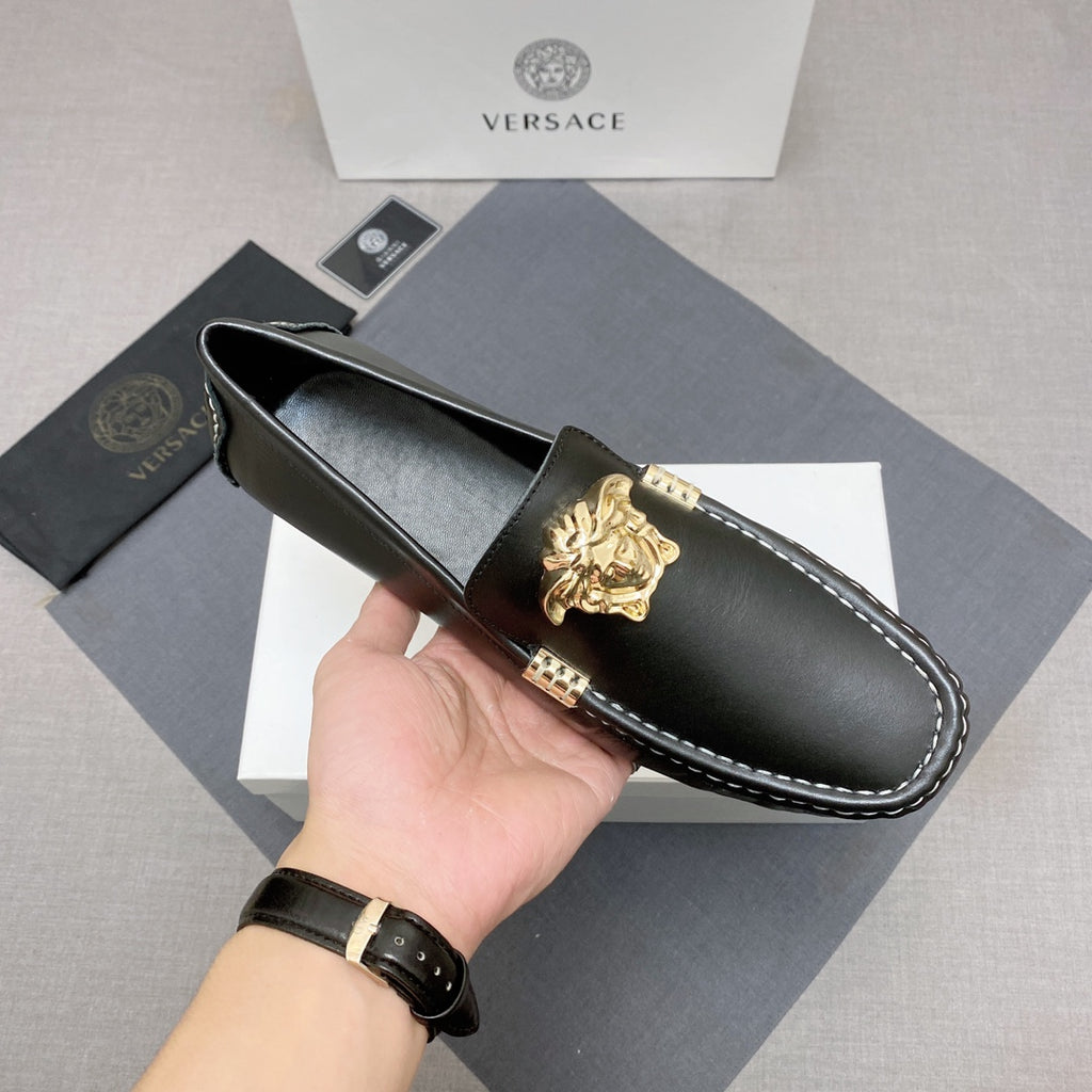 Versace black leather loafer held by hand, gold lion medallion and white contrast stitching
