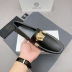 Versace black leather loafer held by hand, gold lion medallion and white contrast stitching