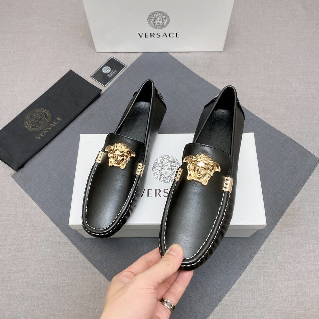 Versace black leather loafer shoes held by hand, gold medallion at the vamp, contrast stitching