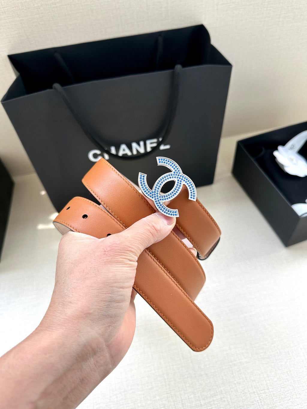 Orange leather belt held up with large blue-and-silver logo buckle