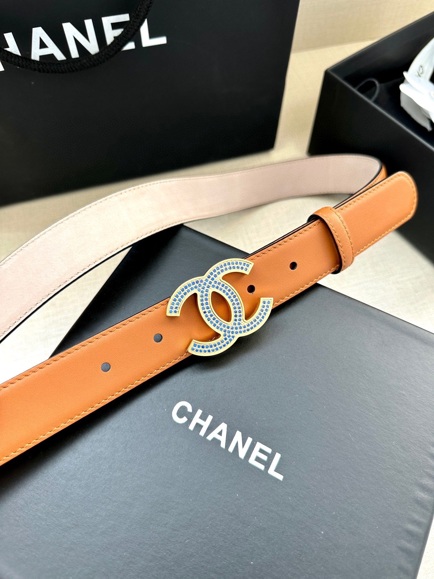 Orange leather belt with blue and silver logo buckle, studded holes on strap