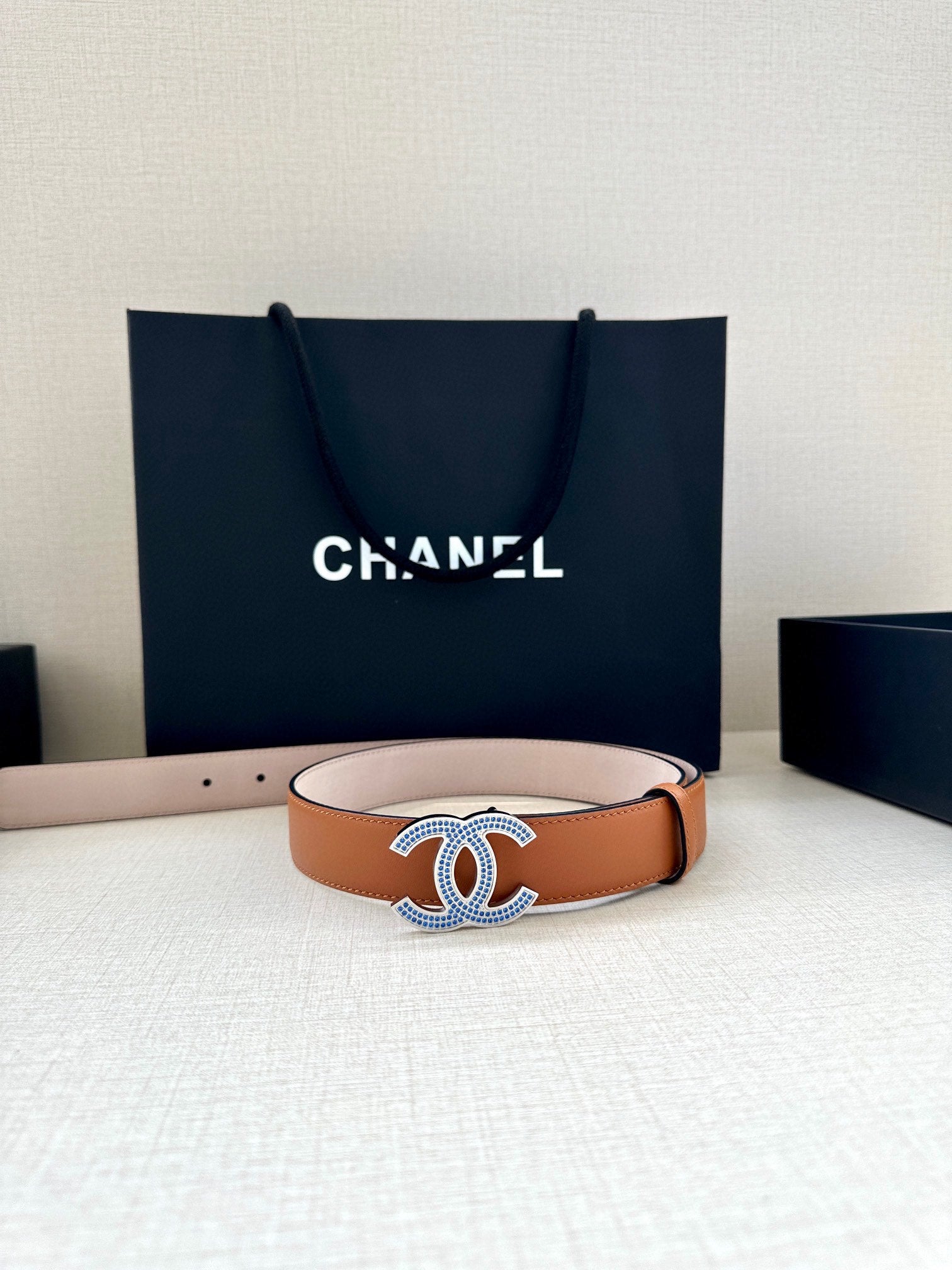 Brown leather belt with silver-and-blue logo buckle and smooth strap edge