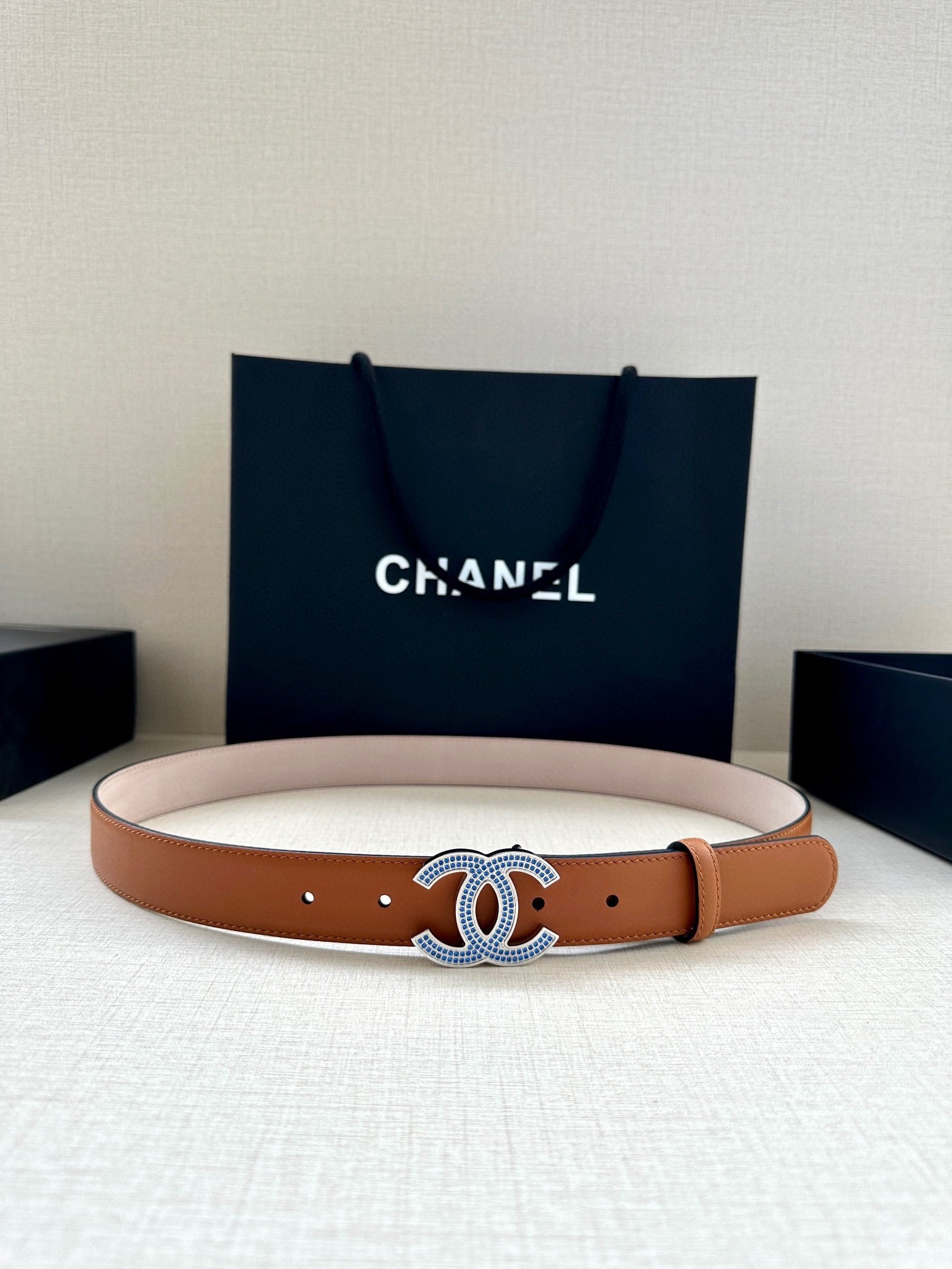 Light tan leather belt with blue and silver logo buckle and round hole markings