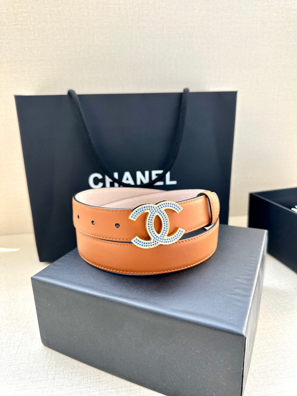 Orange leather belt with oversized logo buckle and multiple adjustment holes