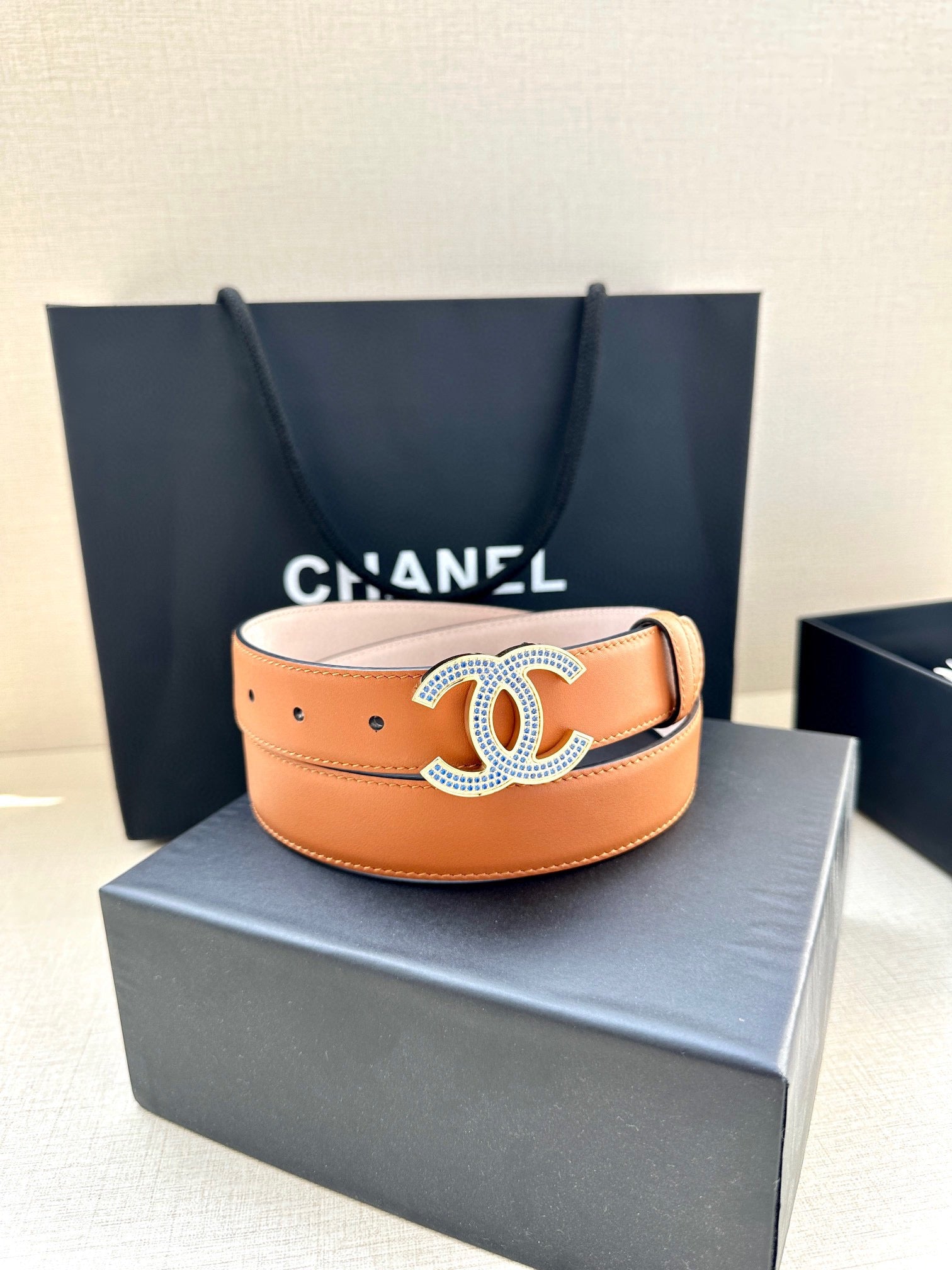 Orange leather belt with oversized logo buckle and multiple adjustment holes