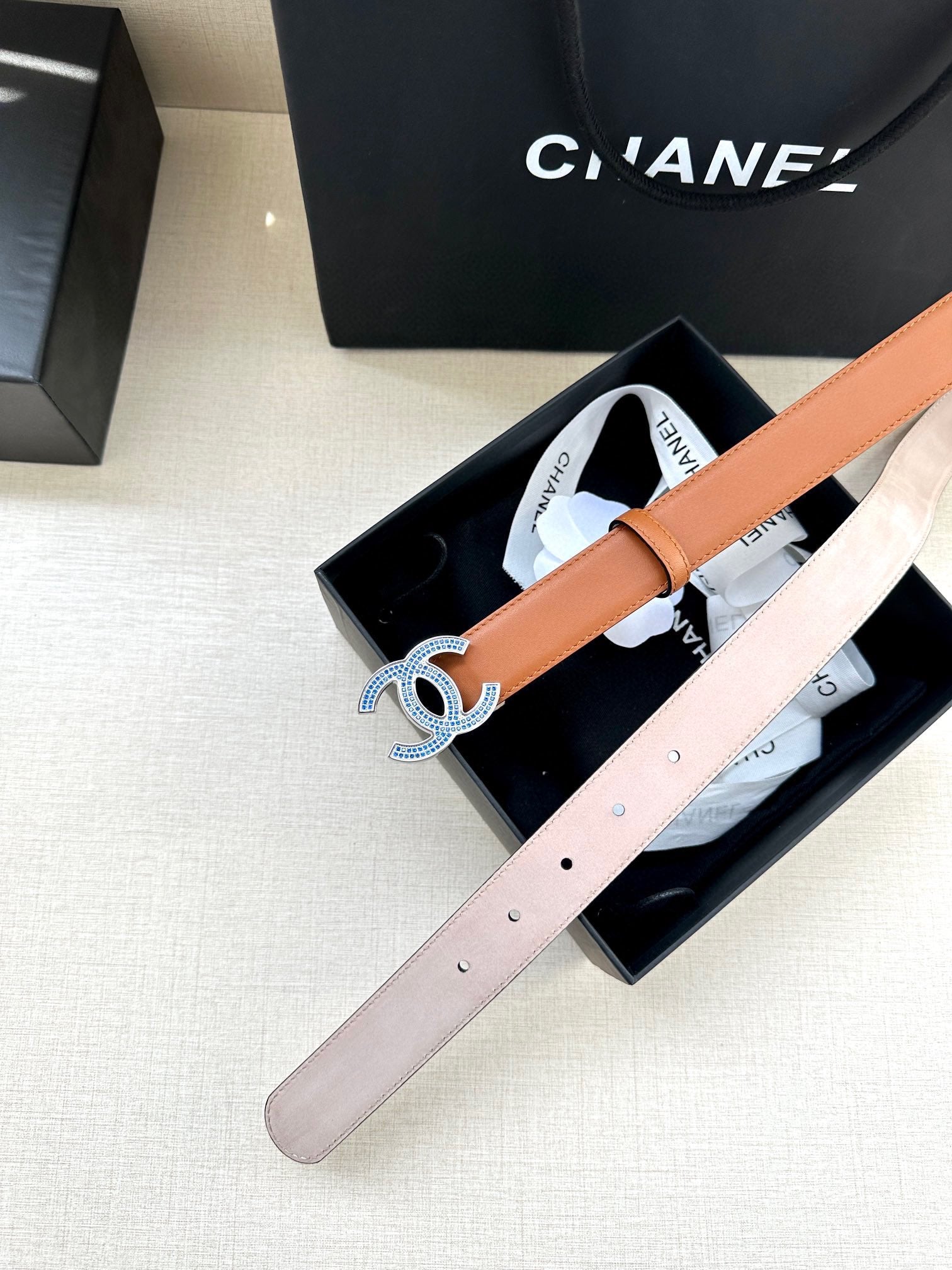 Light pink leather belt with blue-and-silver logo buckle, shown in box