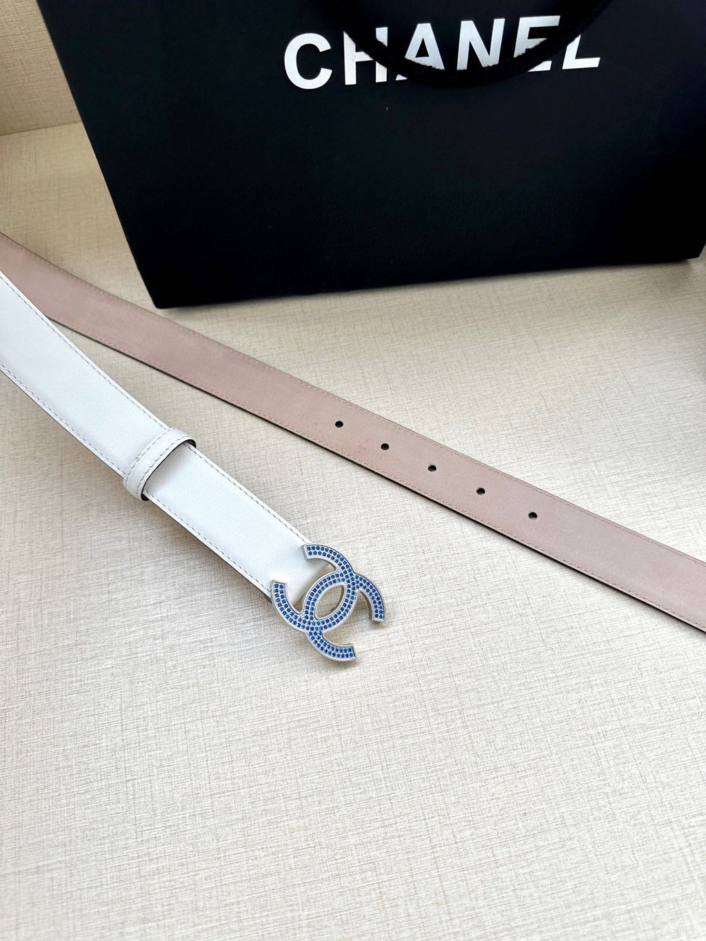 Chanel belt pair laid flat: white and pale pink straps with blue crystal CC buckle