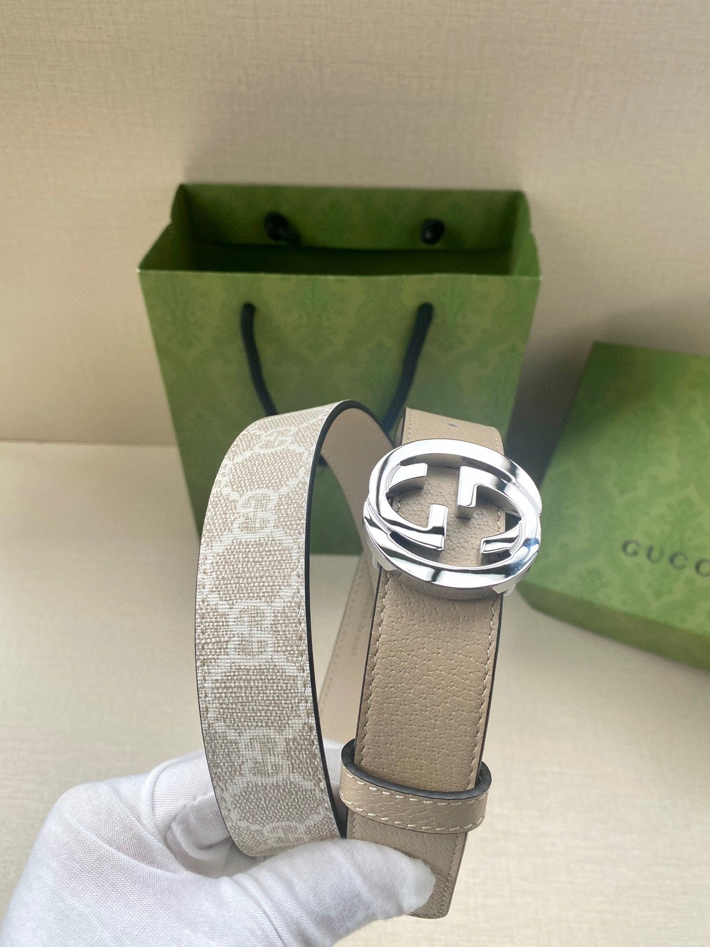Beige leather belt with circular silver-tone GG buckle; monogram fabric end shows