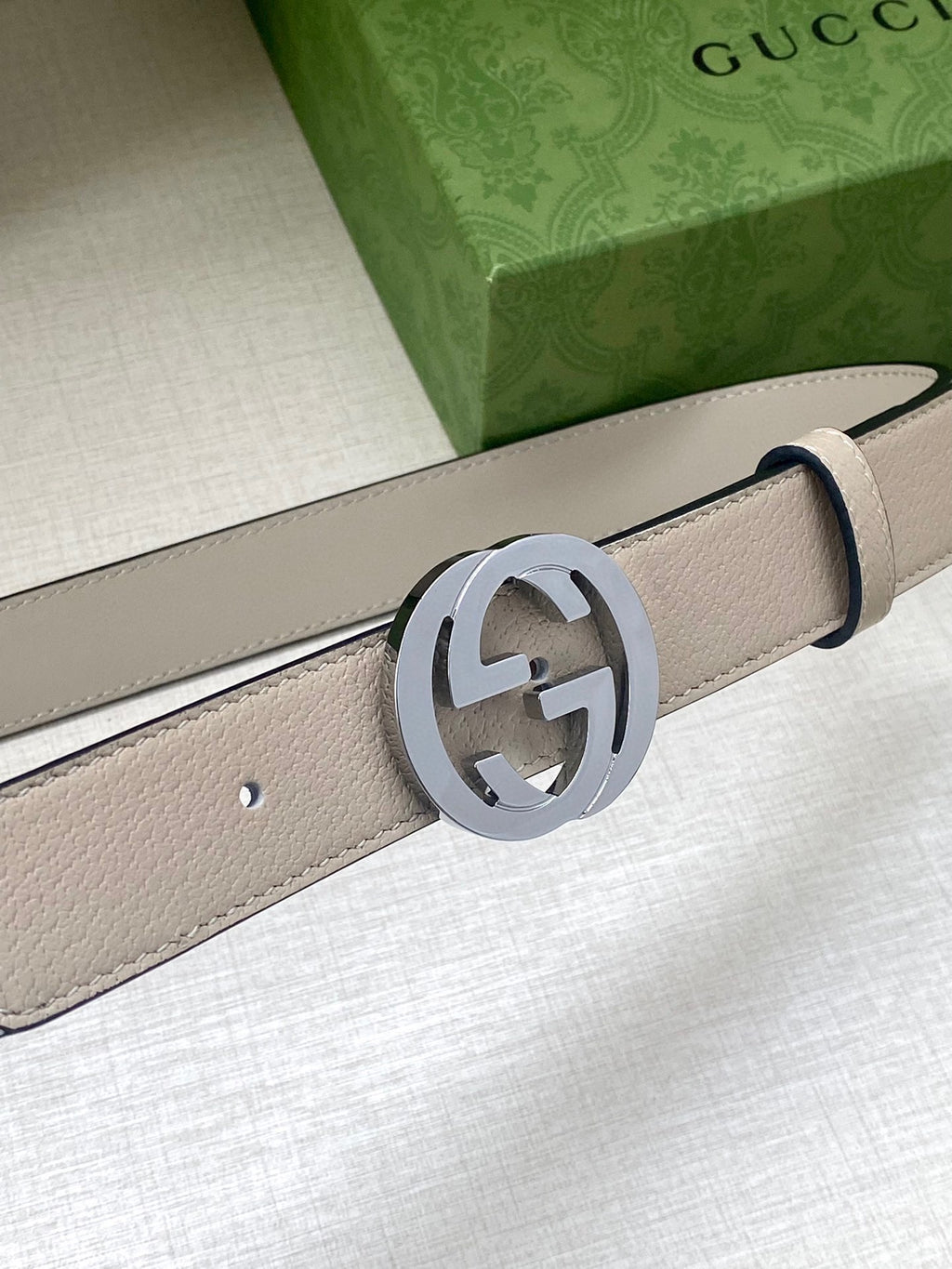 Beige leather belt close-up with round silver-tone GG buckle and stitching detail